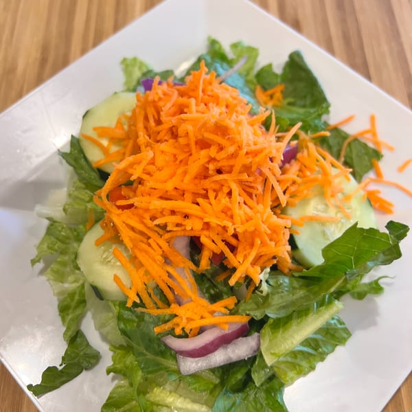 A fresh Greek salad with lettuce, cucumbers, red onions, and shredded carrots on a white plate.
