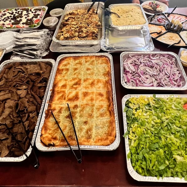 A buffet of Kalamaki Greek food, including gyros meat, spanakopita, rice, salads, and dips.