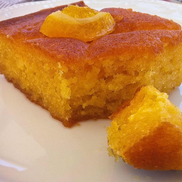 A Greek orange cake, Portokalopita, with a piece broken off, on a white plate.