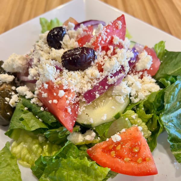 A vibrant Greek salad with lettuce, tomatoes, cucumbers, red onions, olives, and feta cheese.