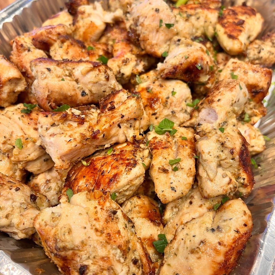 Close-up of Kalamaki's grilled chicken pieces, seasoned with herbs and spices, in a foil tray.