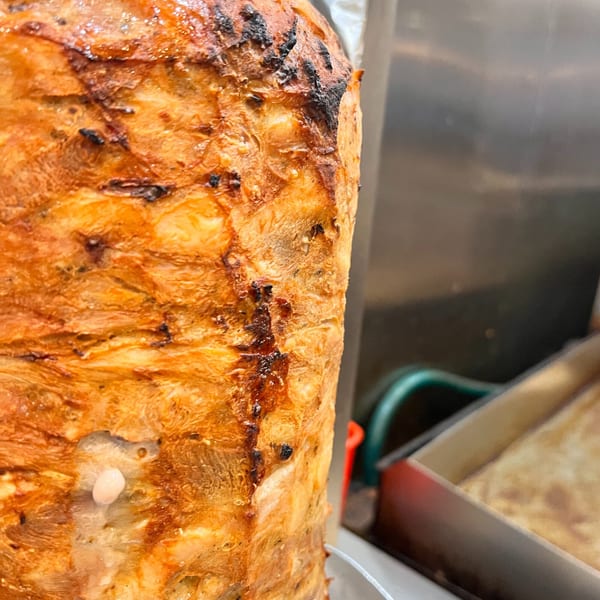 Close-up of a large, rotating vertical spit of golden-brown Greek gyros meat.