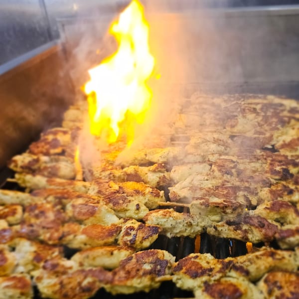 Chicken souvlaki skewers grilling over open flames and smoke at Kalamaki.