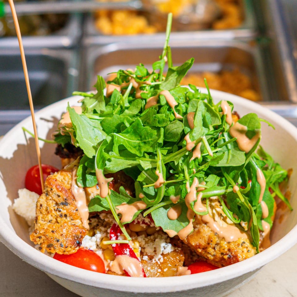 Kalamaki Greek bowl with chicken, arugula, cherry tomatoes, feta, and a creamy sauce.