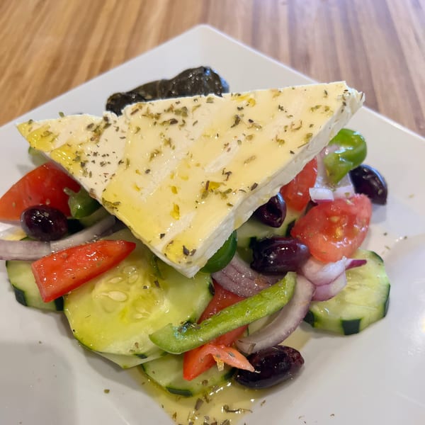 A Kalamaki Greek salad with a large feta slice, tomatoes, cucumbers, olives, and red onions.