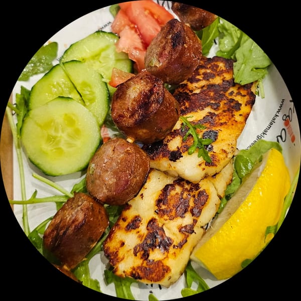 Grilled halloumi cheese and Greek meatballs with cucumber, tomato, arugula, and a lemon wedge.