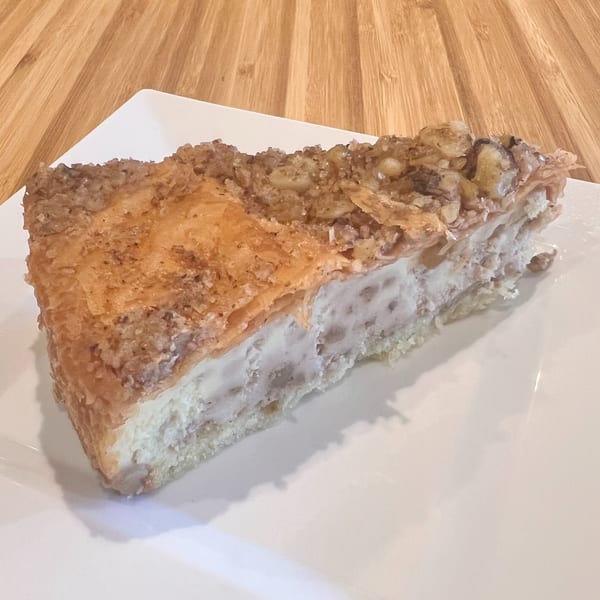 A slice of Greek galaktoboureko, a custard-filled pastry with a crispy, nutty top, on a white plate.