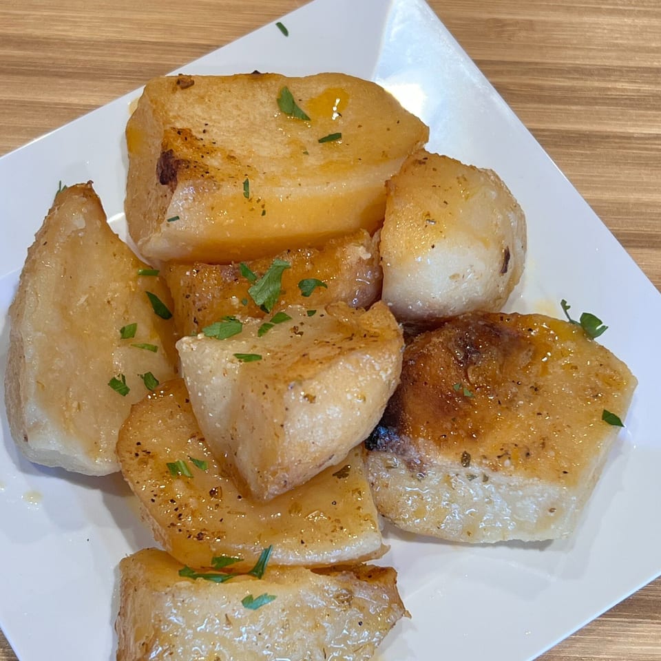 Golden-brown Greek roasted potatoes, drizzled with olive oil and sprinkled with fresh parsley on a white plate.